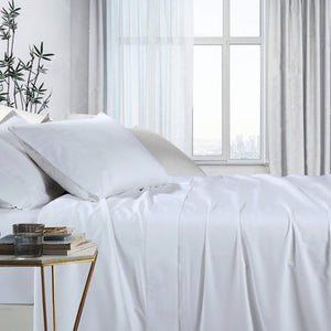 A white, double-sized bed sheet set displayed in a bedroom setting with a fitted sheet, flat sheet, and pillowcases visible.