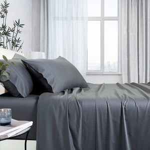 A charcoal-colored sheet set on a bed, with a fitted sheet, flat sheet, and pillowcases displayed in a room with window in the background.
