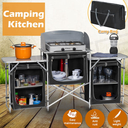 A foldable camping kitchen with a built-in cupboard and bench, set up on a wooden surface. It includes a portable stove, pots, plates, and other kitchen utensils.