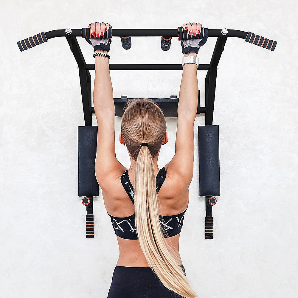 Woman performing pull-ups on a black pull-up bar against a white wall