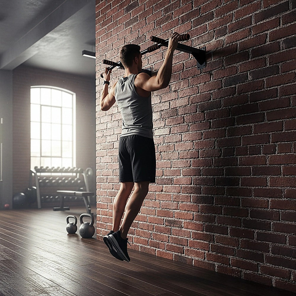 Person doing pull-ups on a bar against a brick wall in a gym.