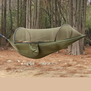 A military green outdoor camping hammock with built-in mosquito net, displayed in an outdoor setting with trees in the background.