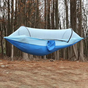 A blue outdoor camping hammock with a built-in mosquito net, displayed in a forest setting.