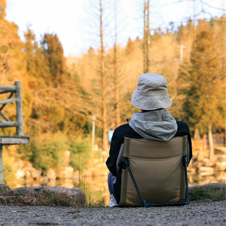 Person sitting in a folding chair by a lake with autumn trees in the background