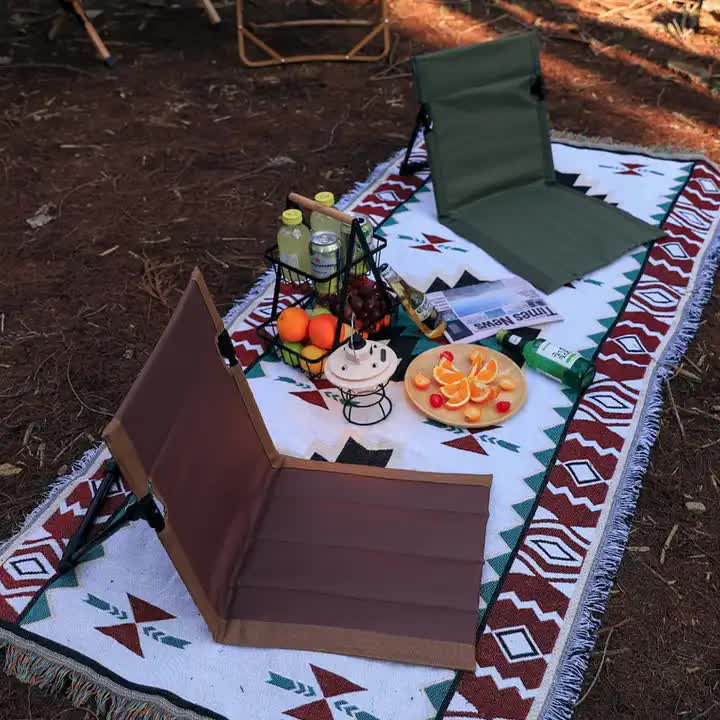 Picnic setup with food, drinks, and a chair on a patterned blanket outdoors.