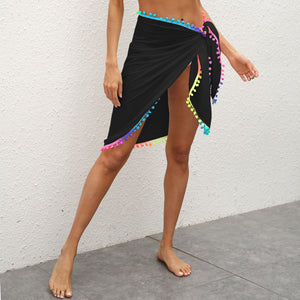 A person wearing a black sarong with colorful tassel trim around the waist.