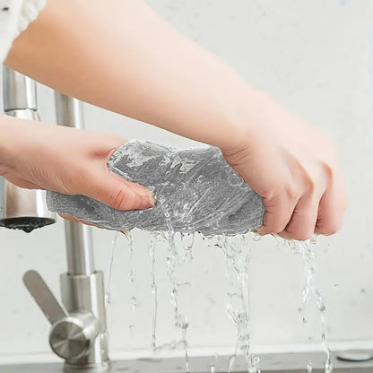 Person washing a gray sponge under running water in a sink.