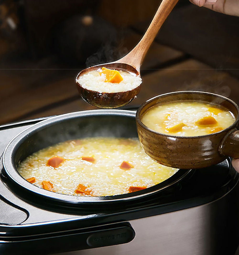 Steaming rice porridge with carrots in a pot, being served with a wooden spoon.
