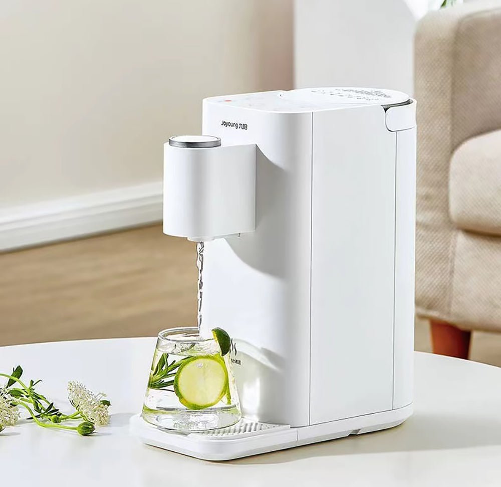 White electric water dispenser pouring water into a glass with lime and mint leaves on a white surface.