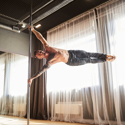 Man performing a pole dance move in a room with curtains and a light fixture.