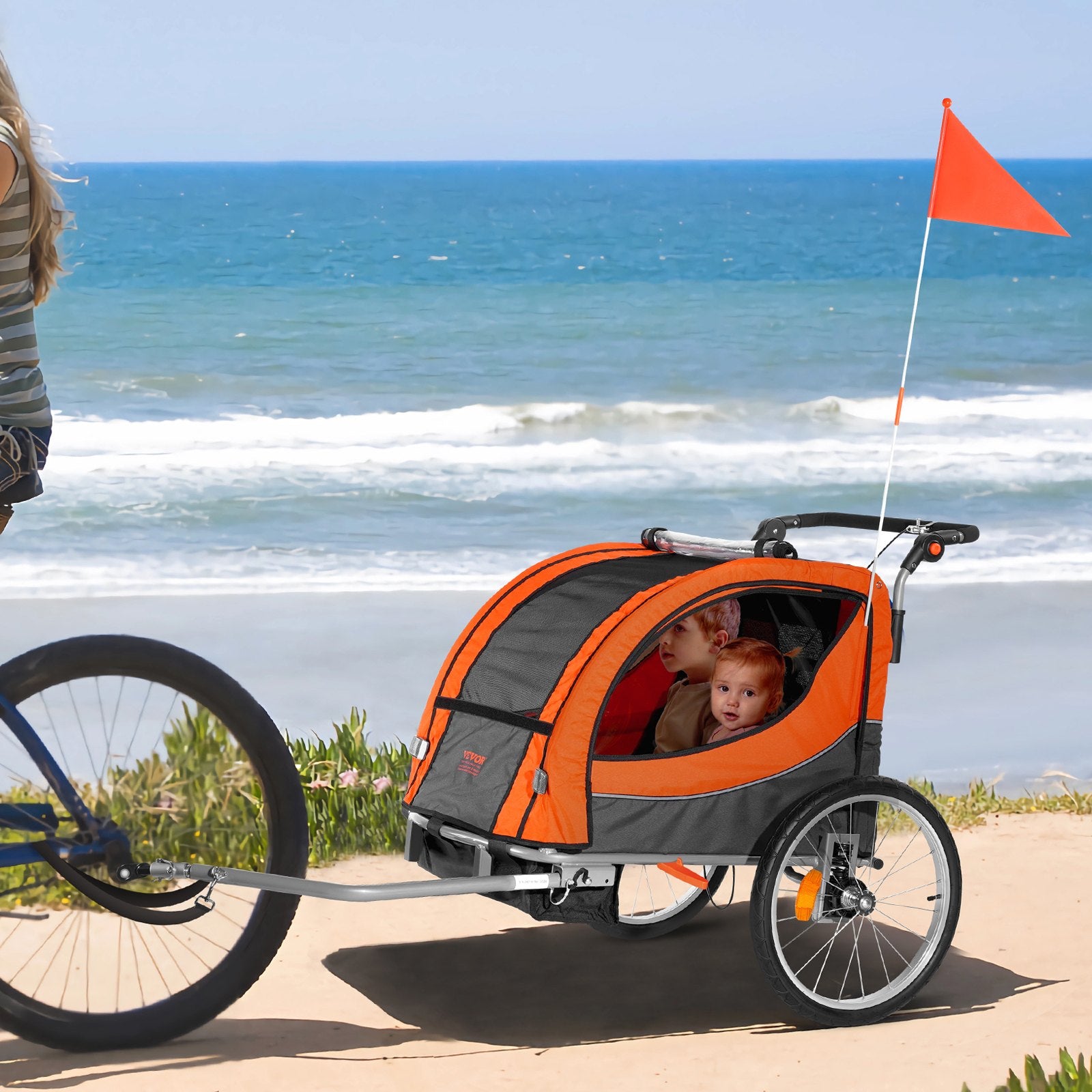 Orange and gray bicycle trailer with two children on a beach.