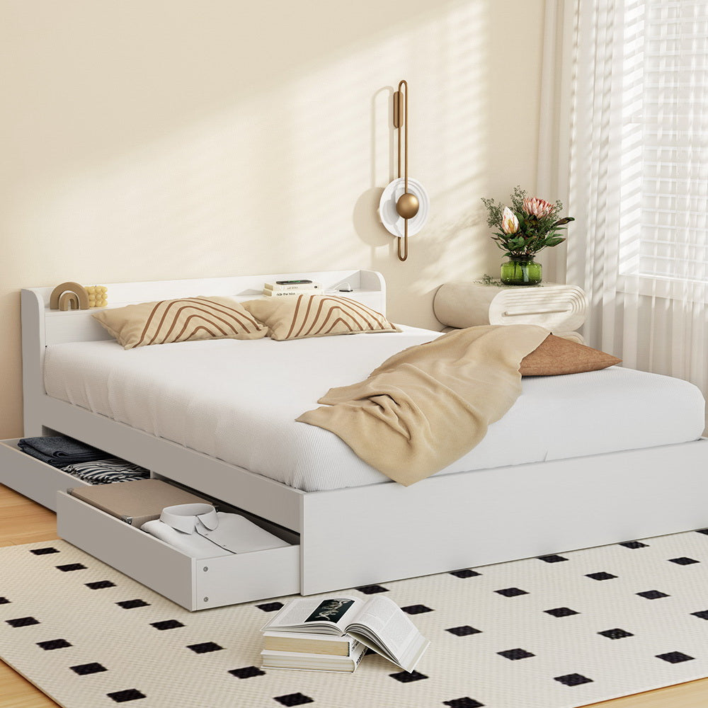 A white Artiss bed frame with storage drawers and USB charging ports, made from particleboard and plywood, in a room setting with bedding and a carpeted floor.