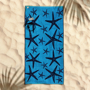 A blue beach towel with a nautical starfish jacquard design laid out on a sandy beach.