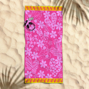 A bright pink beach towel with a floral and nautical jacquard design laid out on a sandy beach with a pair of sunglasses on top.